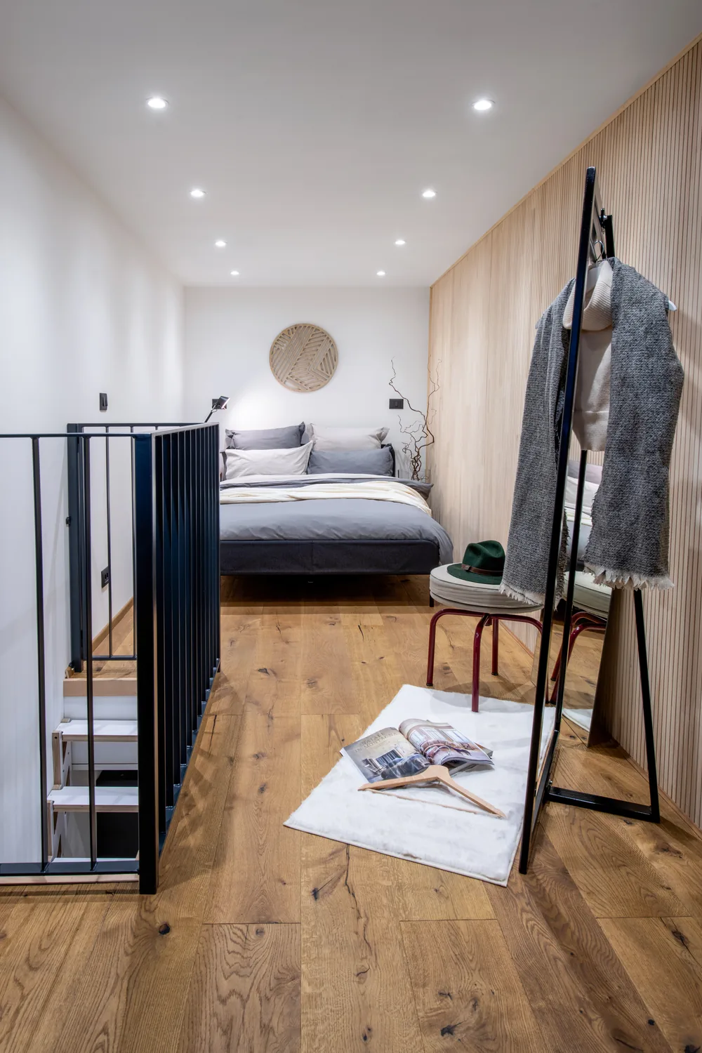 Schlafzimmer im Obergeschoss mit Bett, Holzwand und schwarzem Geländer über der Treppe