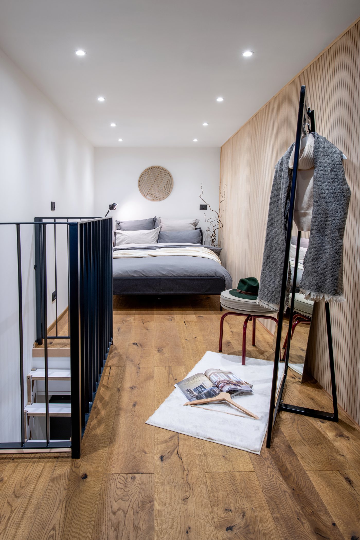Schlafzimmer im Obergeschoss mit Bett, Holzwand und schwarzem Geländer über der Treppe