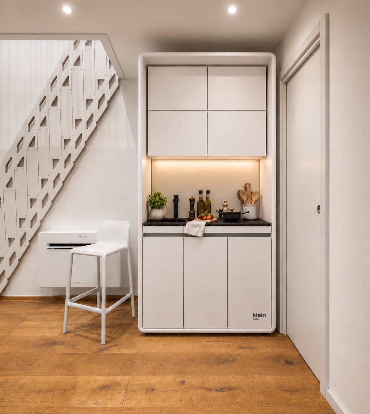Die KleinCASA-Küche neben der Treppe: kompakter weisser Küchenblock mit dunkler Arbeitsplatte, Hängeschränken und weissem Hocker