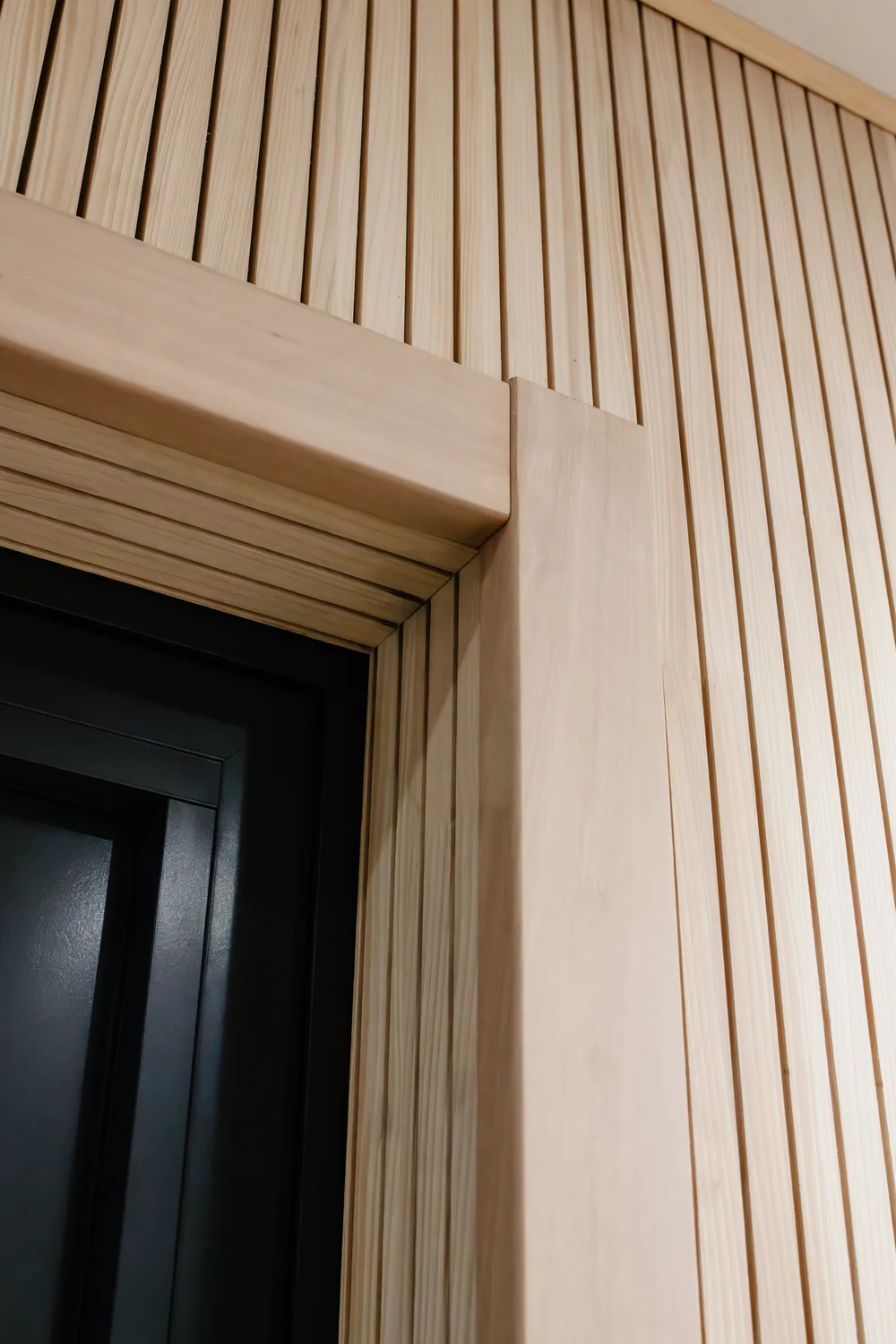 Detail des dunklen Türrahmens, eingelassen in die Wand aus Holzlatten