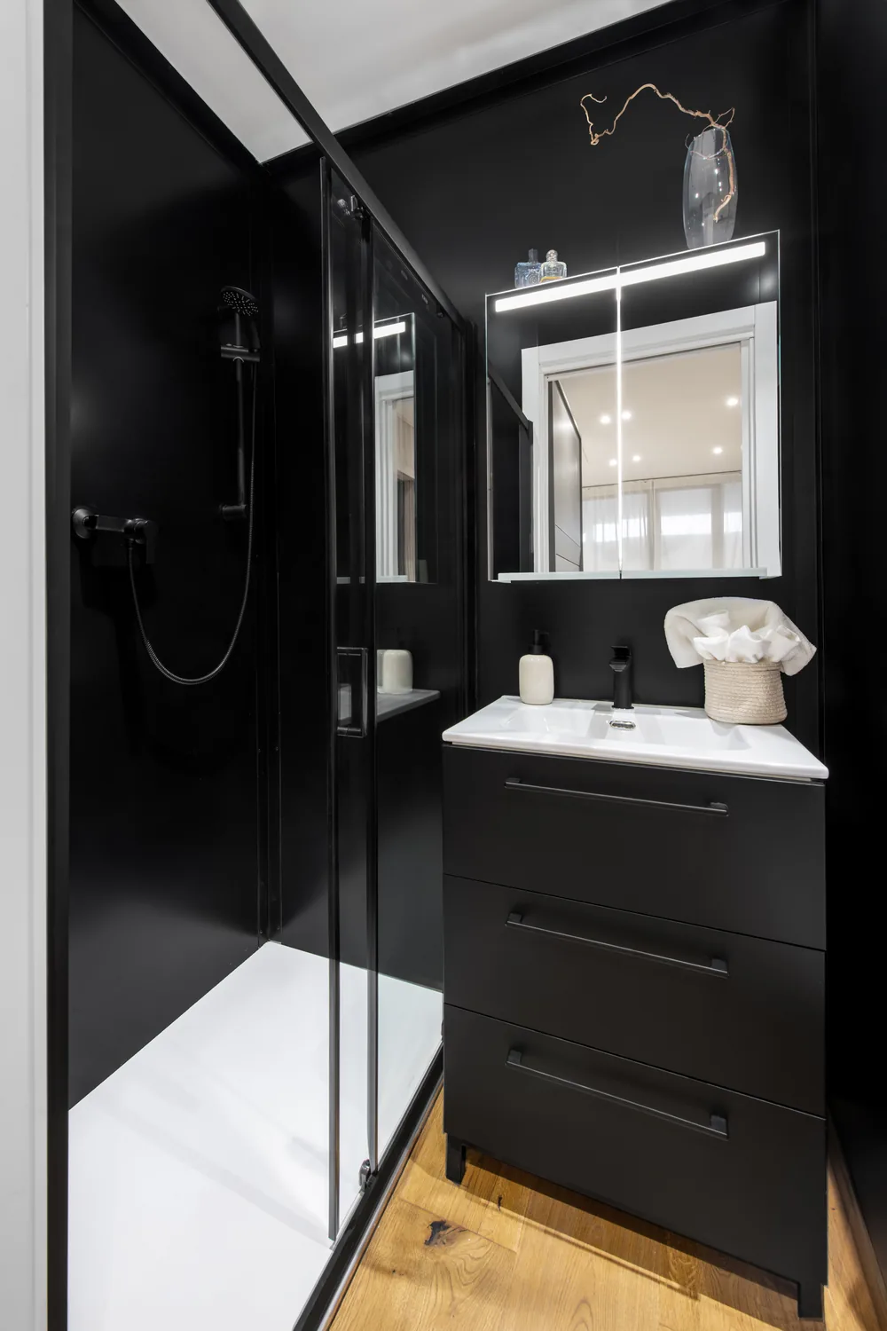 Schwarzes Bad mit raumhoher Dusche, Waschbecken, Möbel und beleuchtetem Spiegel