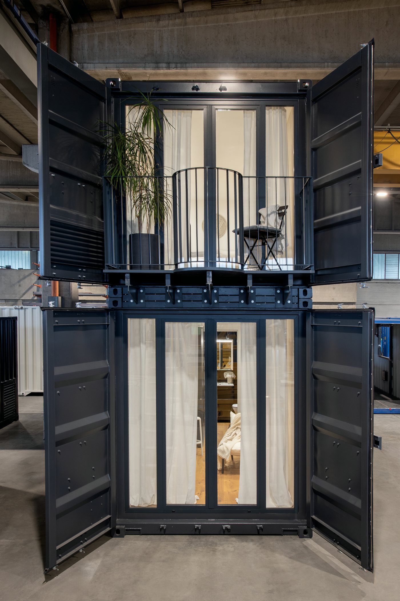 Zweistöckiger Container mit offenen Türen, Balkon und hellen Vorhängen, von vorne in der Werkstatt fotografiert